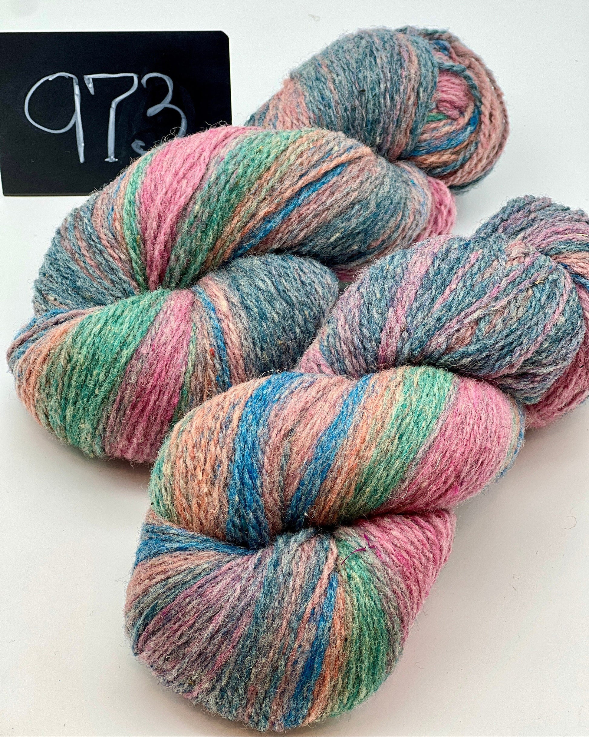 Multicolored skeins of yarn on a white background with a label reading '973'.