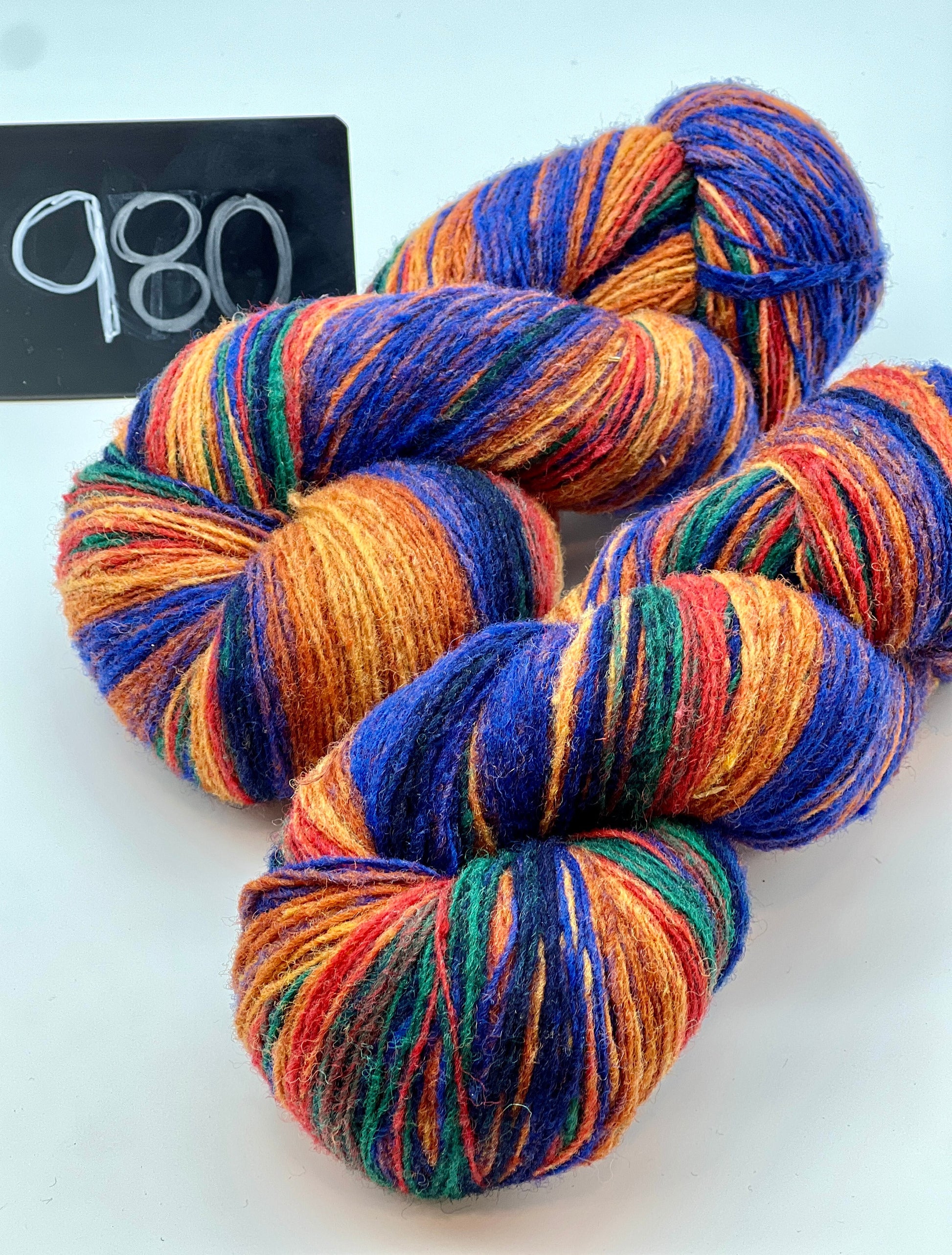 Multicolored yarn skeins on a white background with a black card displaying '980'.