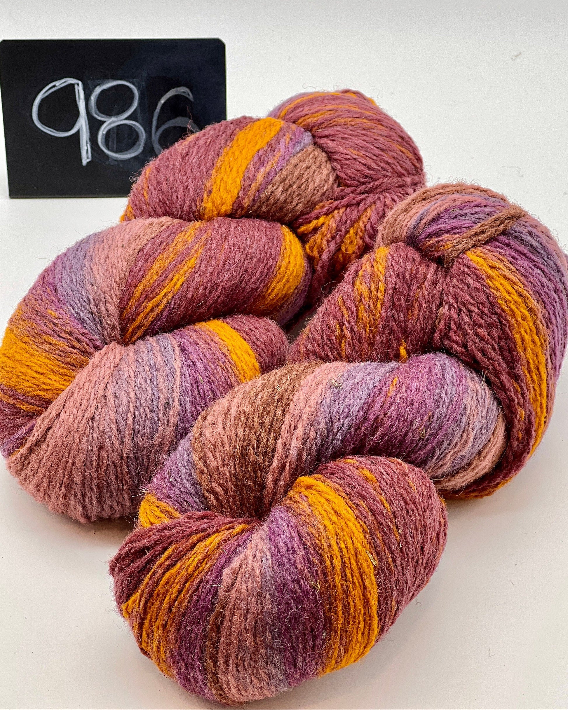 Three skeins of multicolored yarn on a white background with a black sign displaying the number 986.