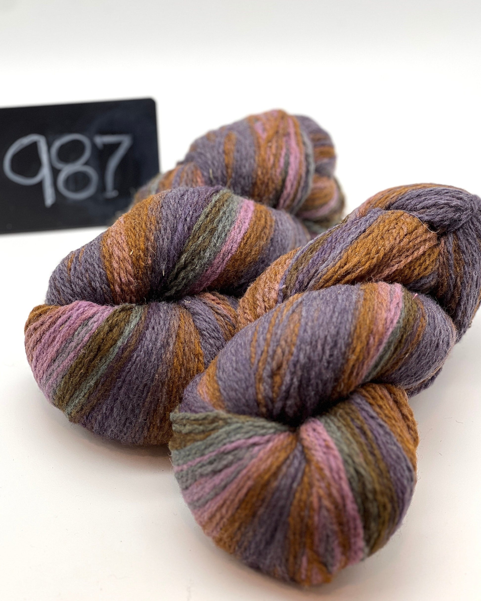 Three skeins of multicolored yarn on a white background with a label reading '987'.