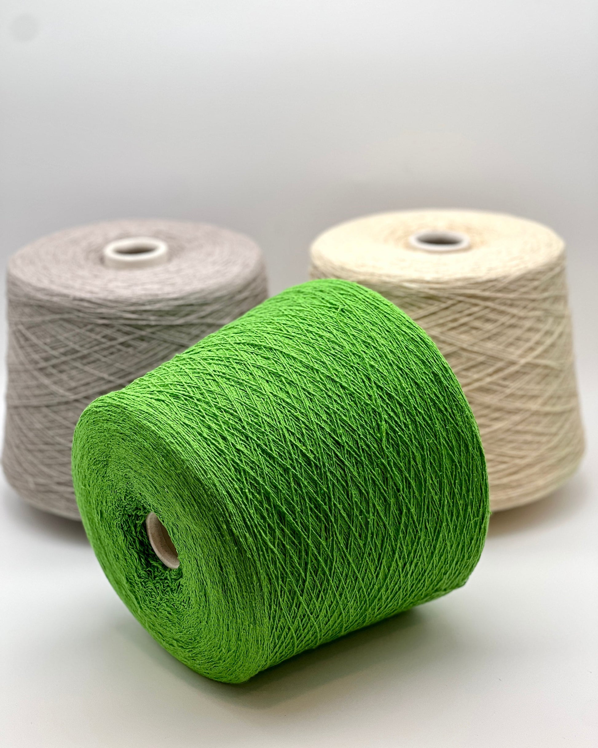 Three spools of yarn in green, gray, and beige on a white background