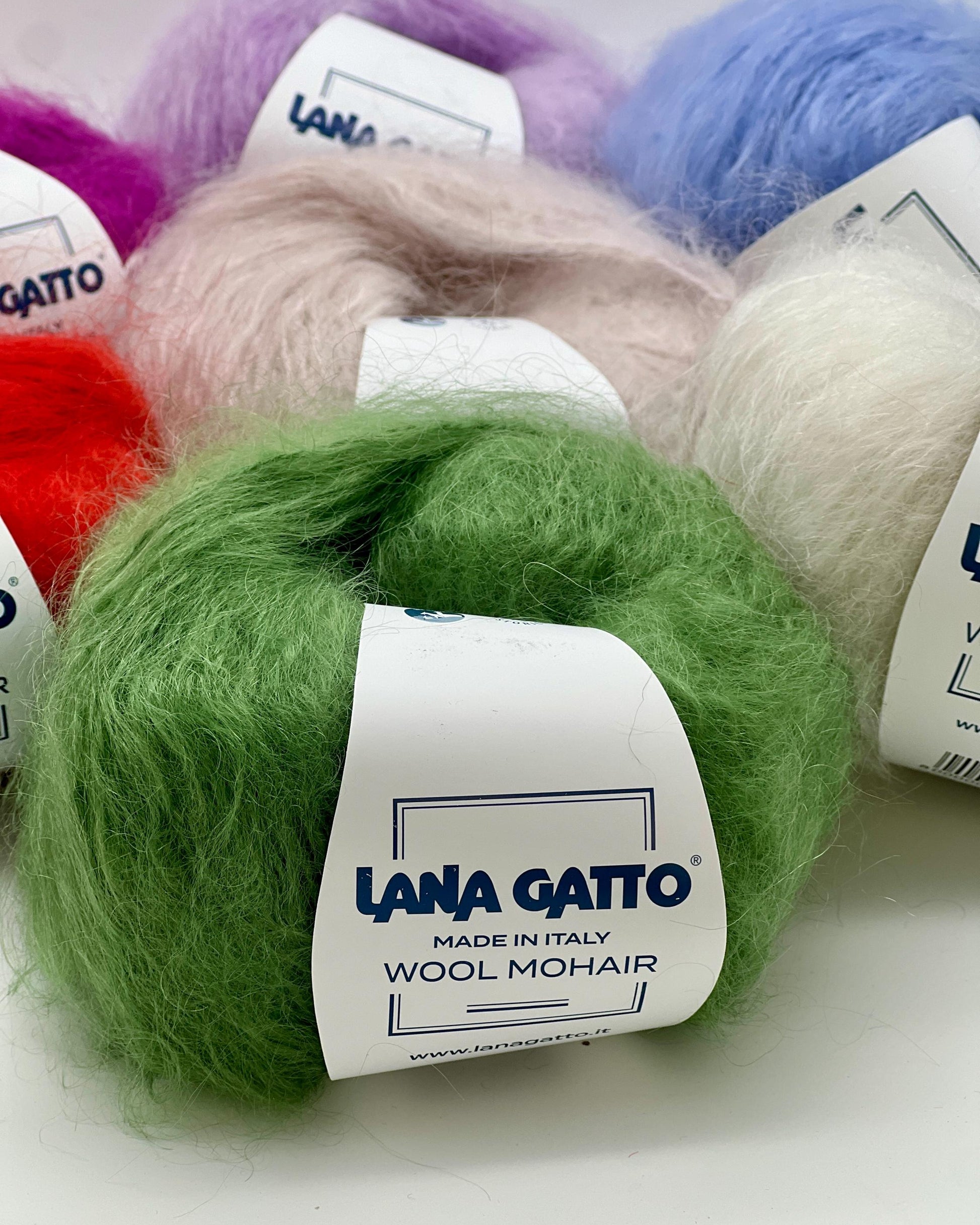 Green ball of Lana Gatto wool mohair yarn with other colored yarns in the background.