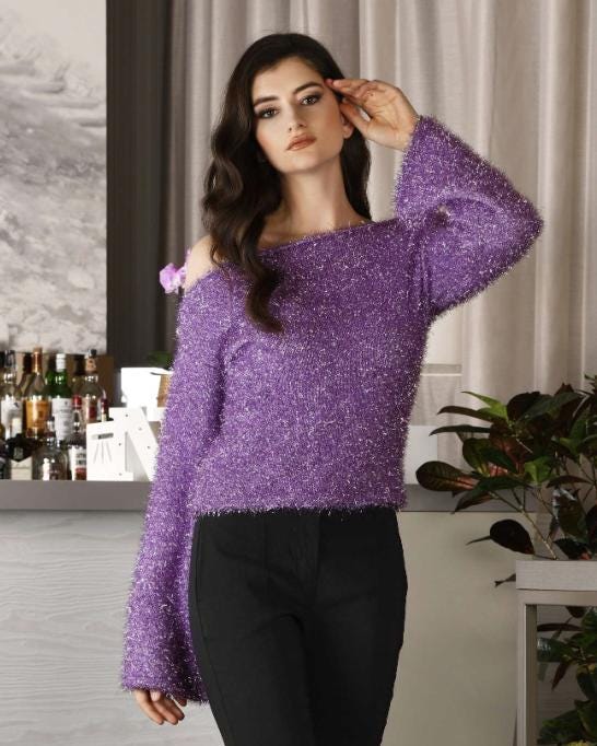 Woman wearing a purple off-shoulder sweater in an indoor setting.