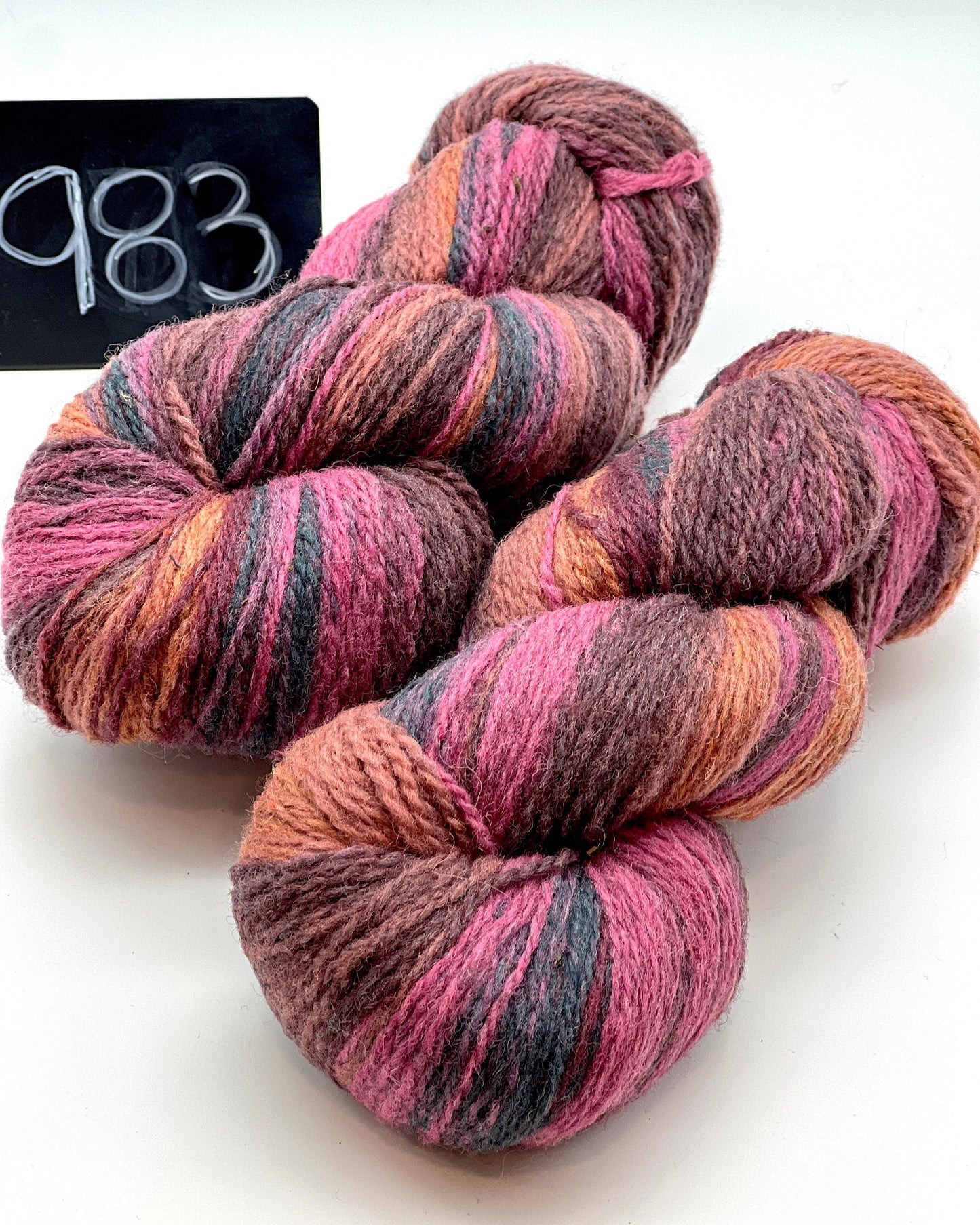 Three skeins of multicolored yarn on a white background with a label reading '983'.