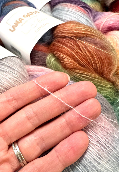 Close-up of colorful yarn with a hand holding a strand, LANA GARTEN branding visible.
