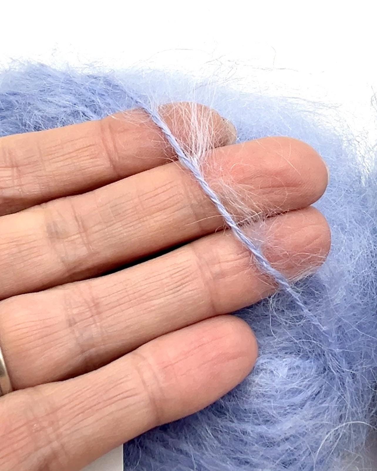 Hand holding a strand of light blue yarn against a white background