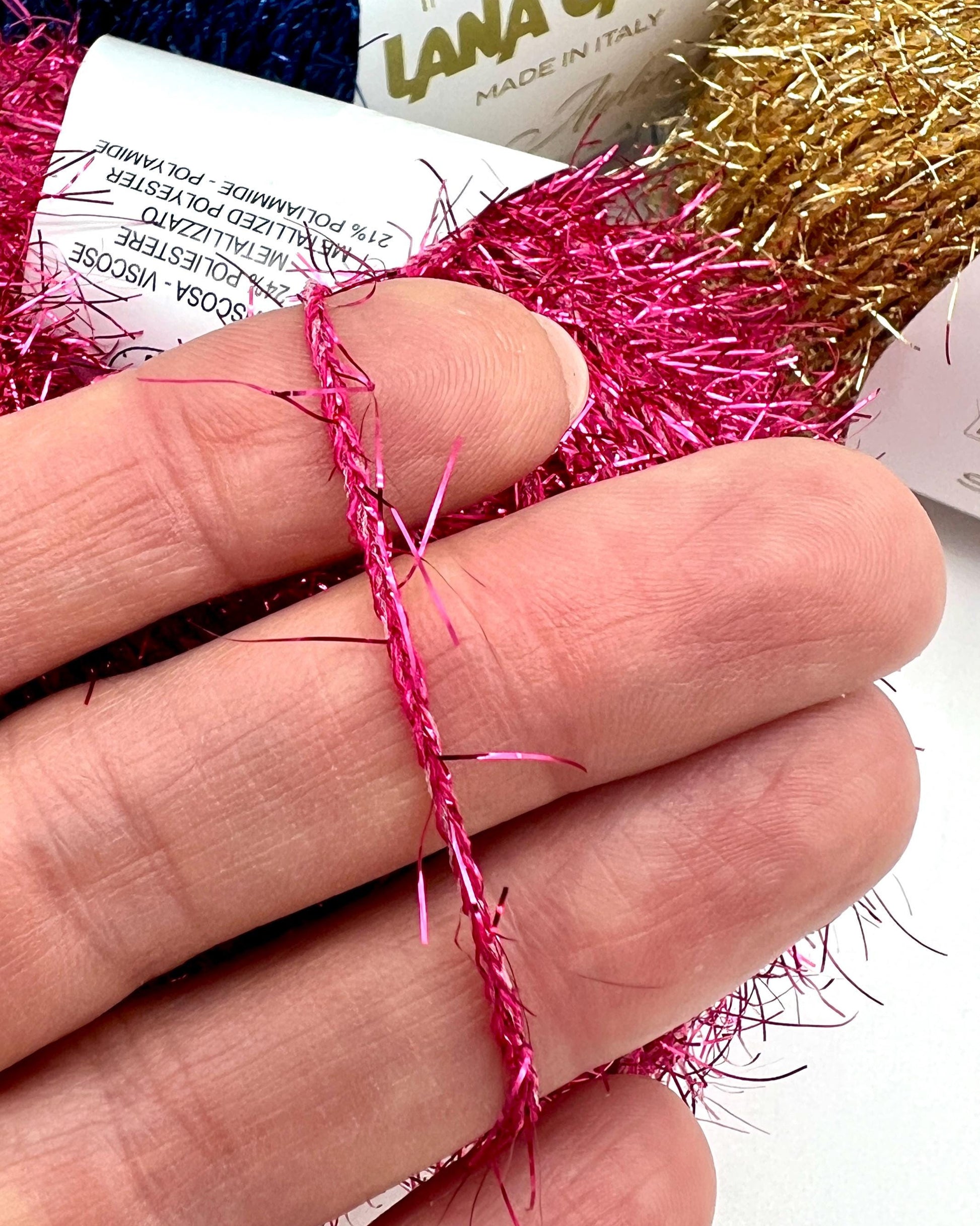 Hand holding pink tinsel with Lana Grossa yarn in the background