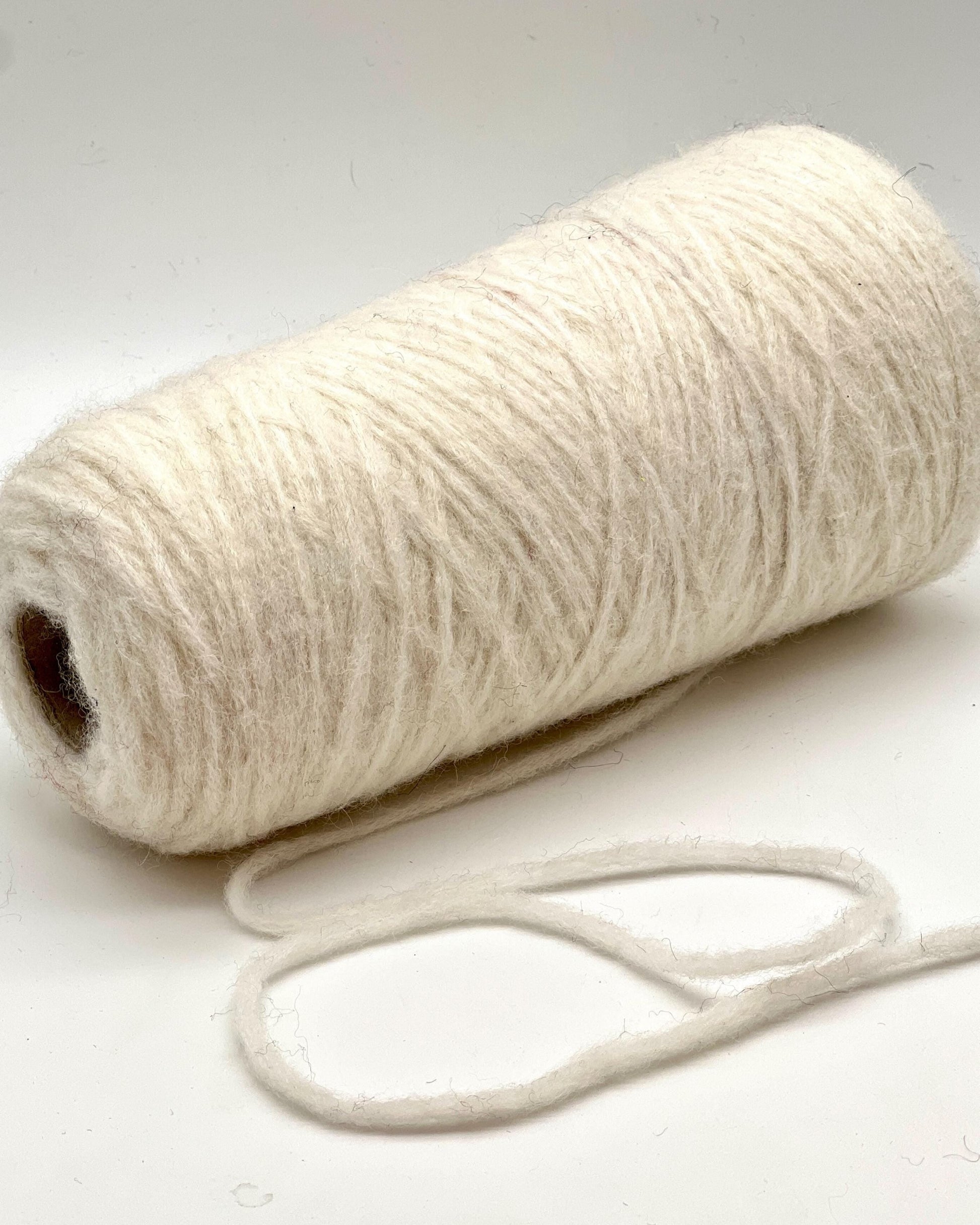Roll of white yarn with a single strand on a light background