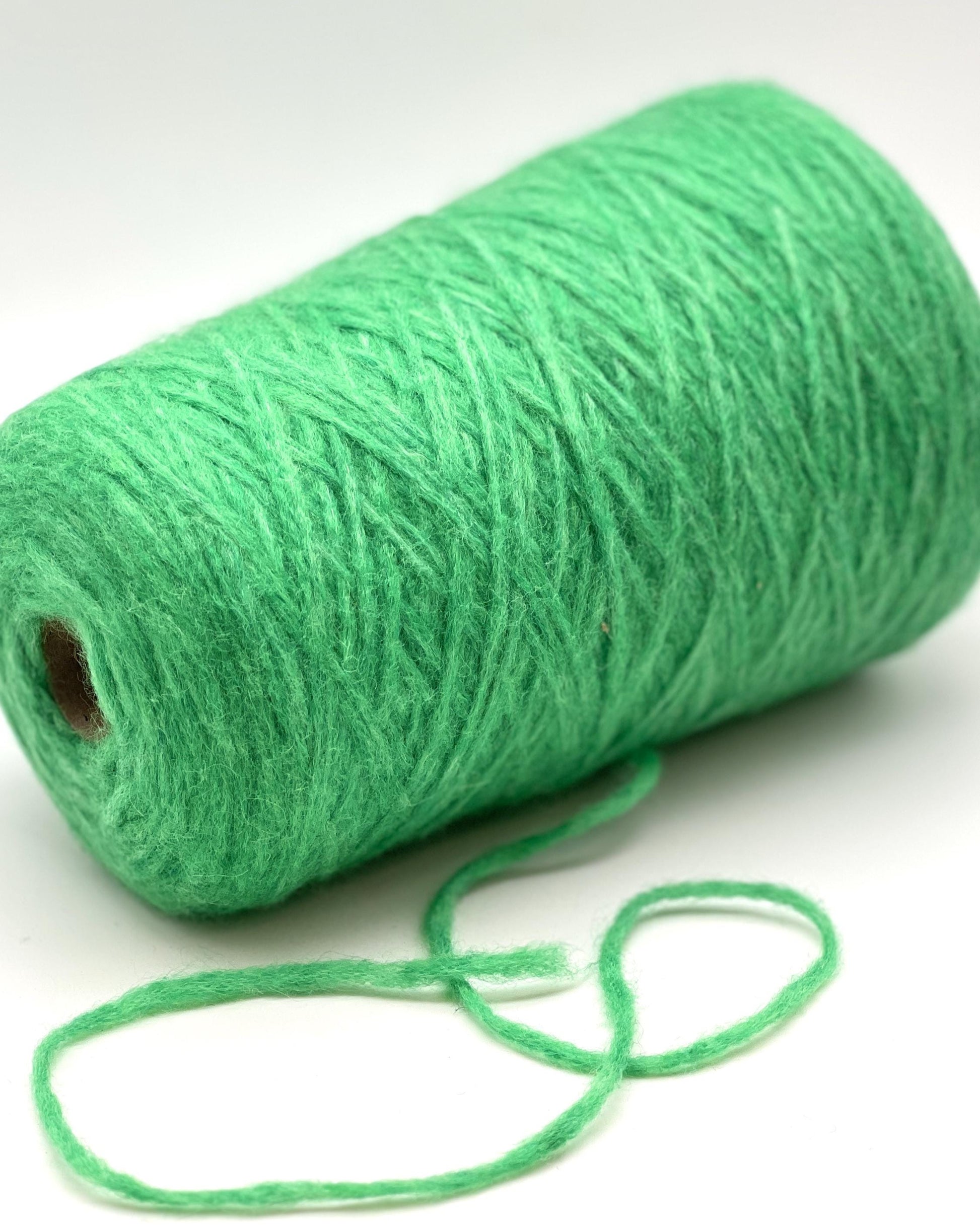 Green yarn roll with a small string on a white background