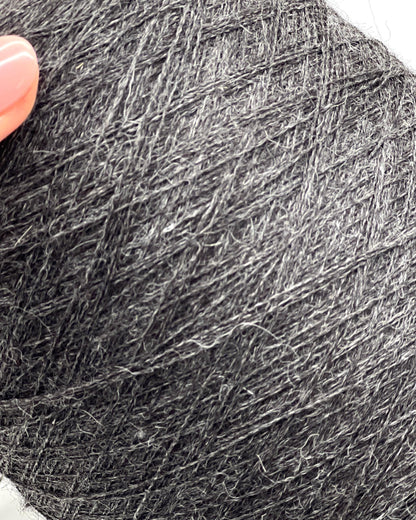 Close-up of a ball of dark gray yarn with a hand holding it.