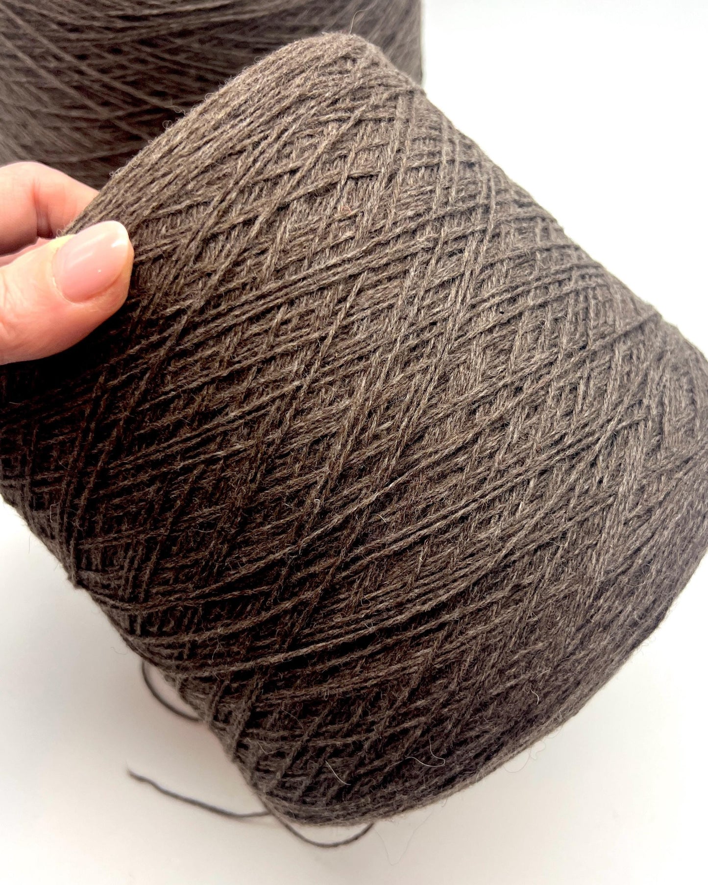 Brown yarn ball held by a hand on a white background