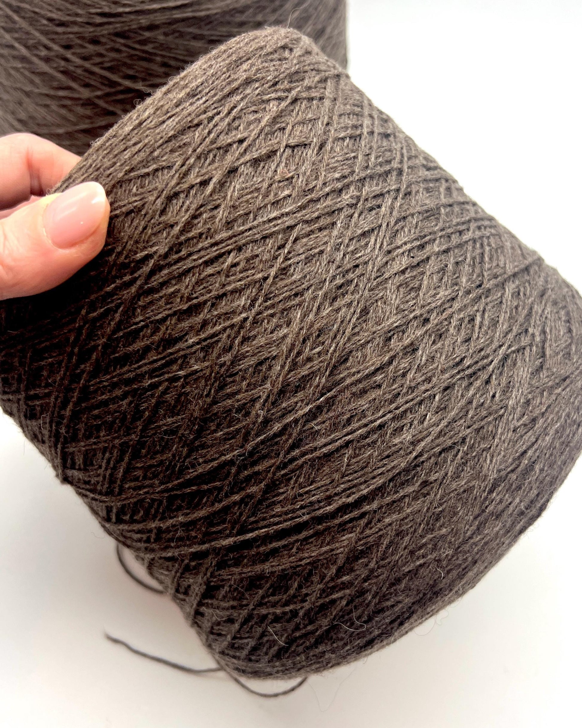 Brown yarn ball held by a hand on a white background