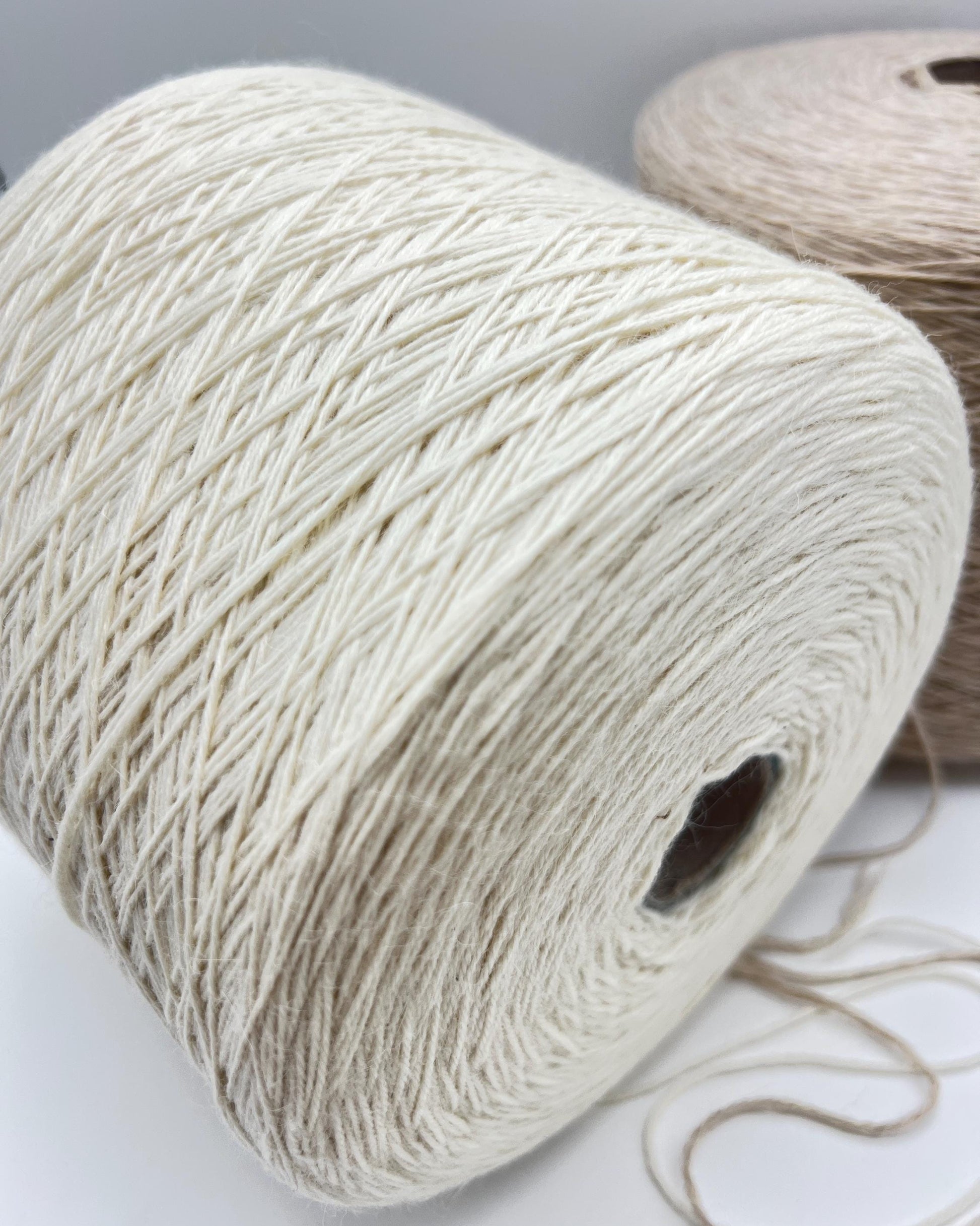 Two spools of yarn, one white and one brown, on a light gray background.