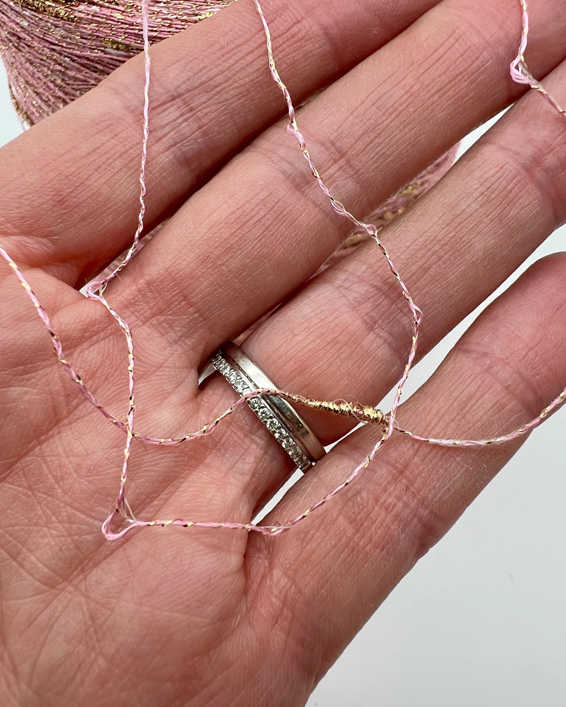 Hand wearing a ring with pink thread woven through the fingers