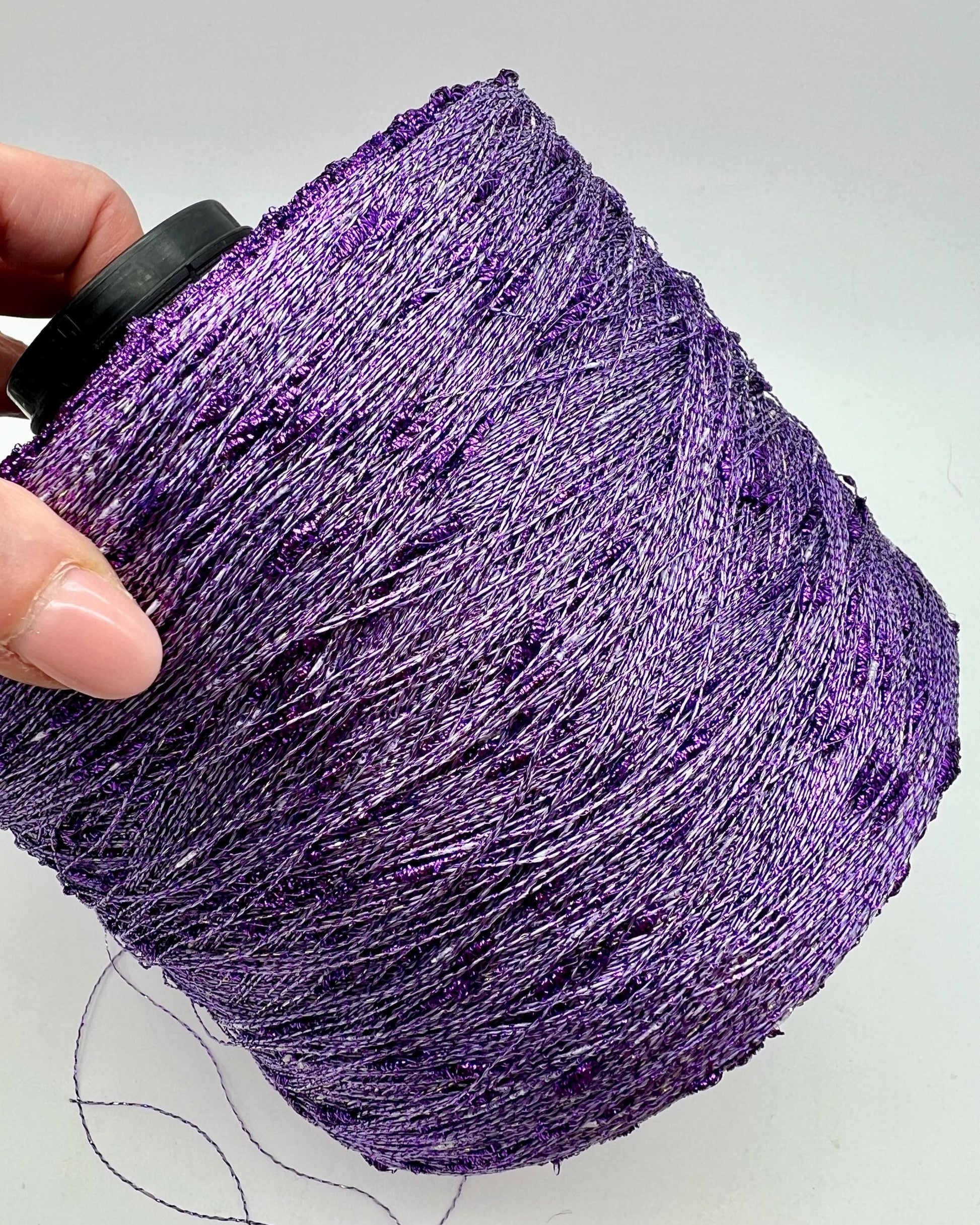 Purple glitter yarn ball held by a hand on a light gray background