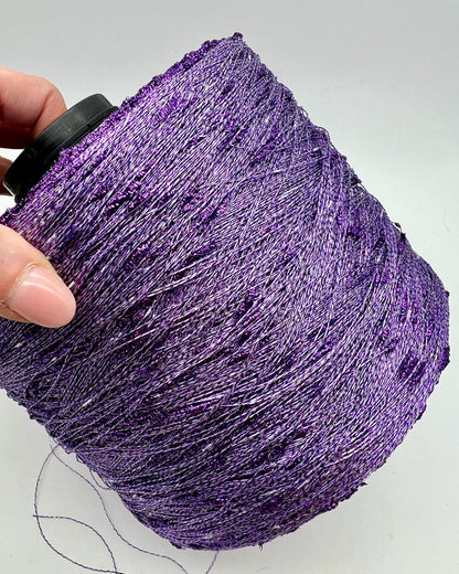 Purple glitter yarn ball held by a hand on a light gray background
