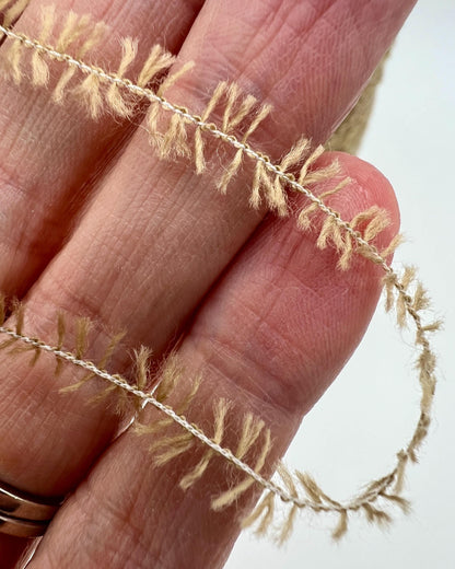 Close-up of a hand holding a delicate, thin branch with small leaves against a light background.