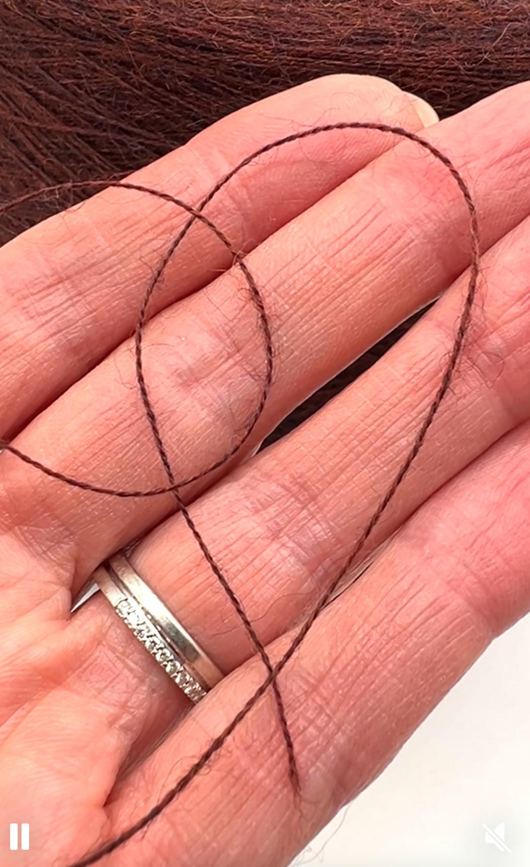 Two thin brown hair strands on a hand with a silver ring.