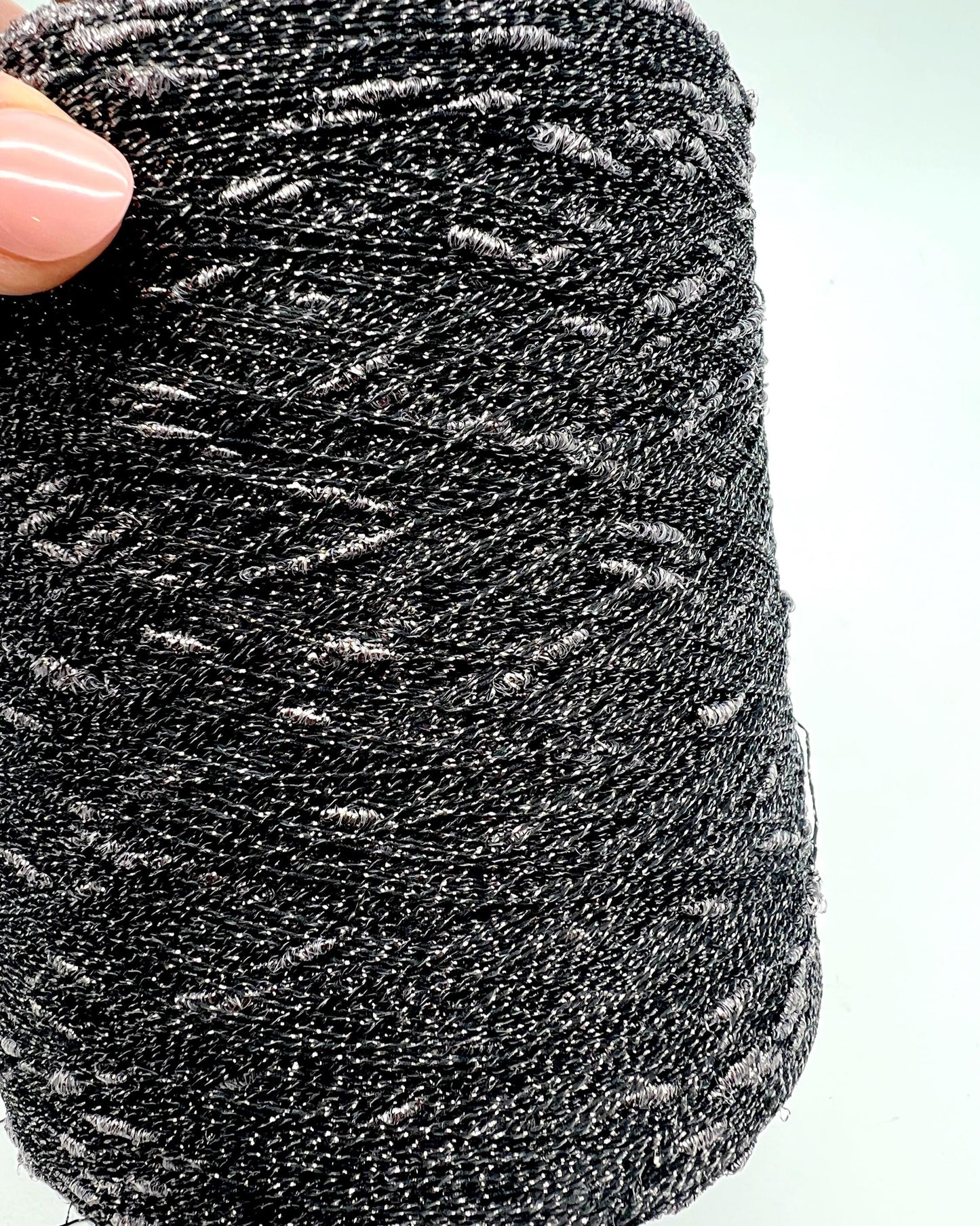 Black glitter yarn held by a hand on a white background