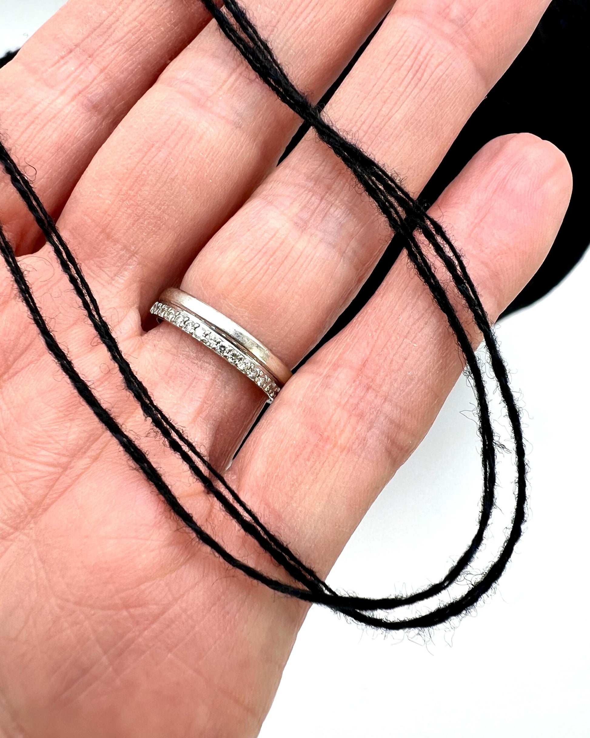 Hand wearing a silver ring with black thread around the fingers on a white background