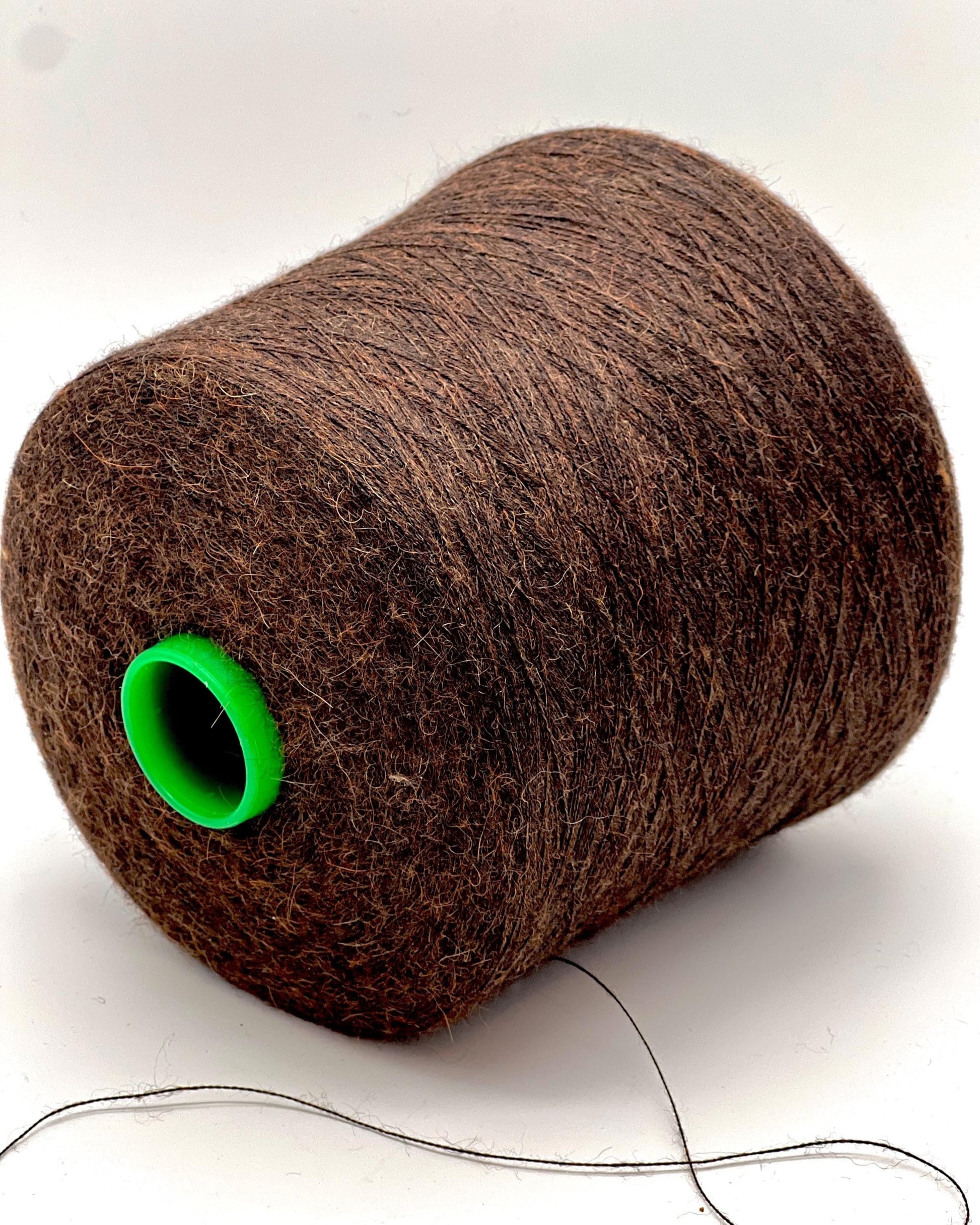 Spool of brown thread with a green end on a white background