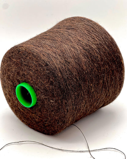 Spool of brown thread with a green end on a white background