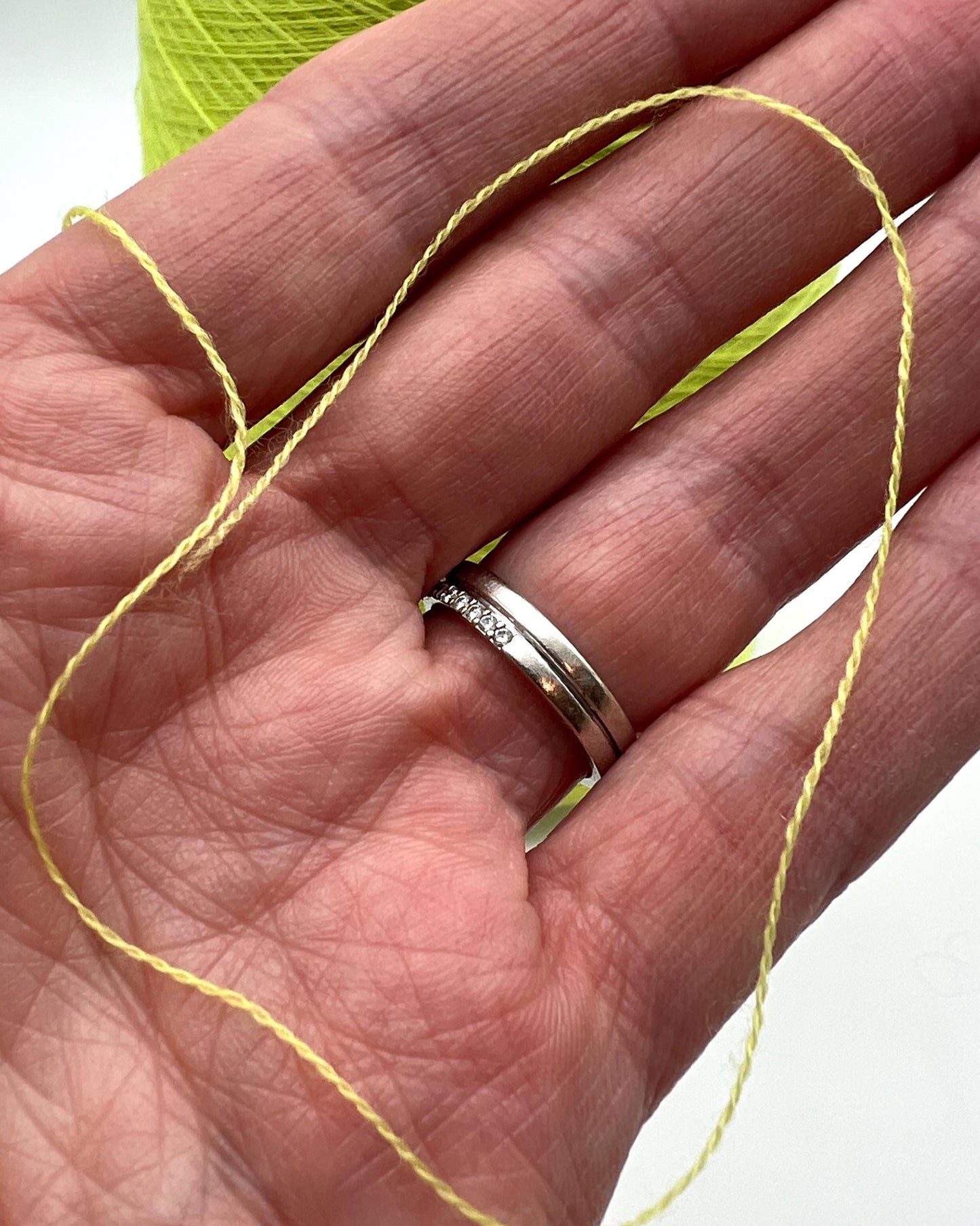 Silver ring on a hand with yellow thread and green yarn in the background