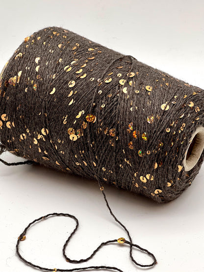 Roll of dark brown yarn with gold sequins on a white background