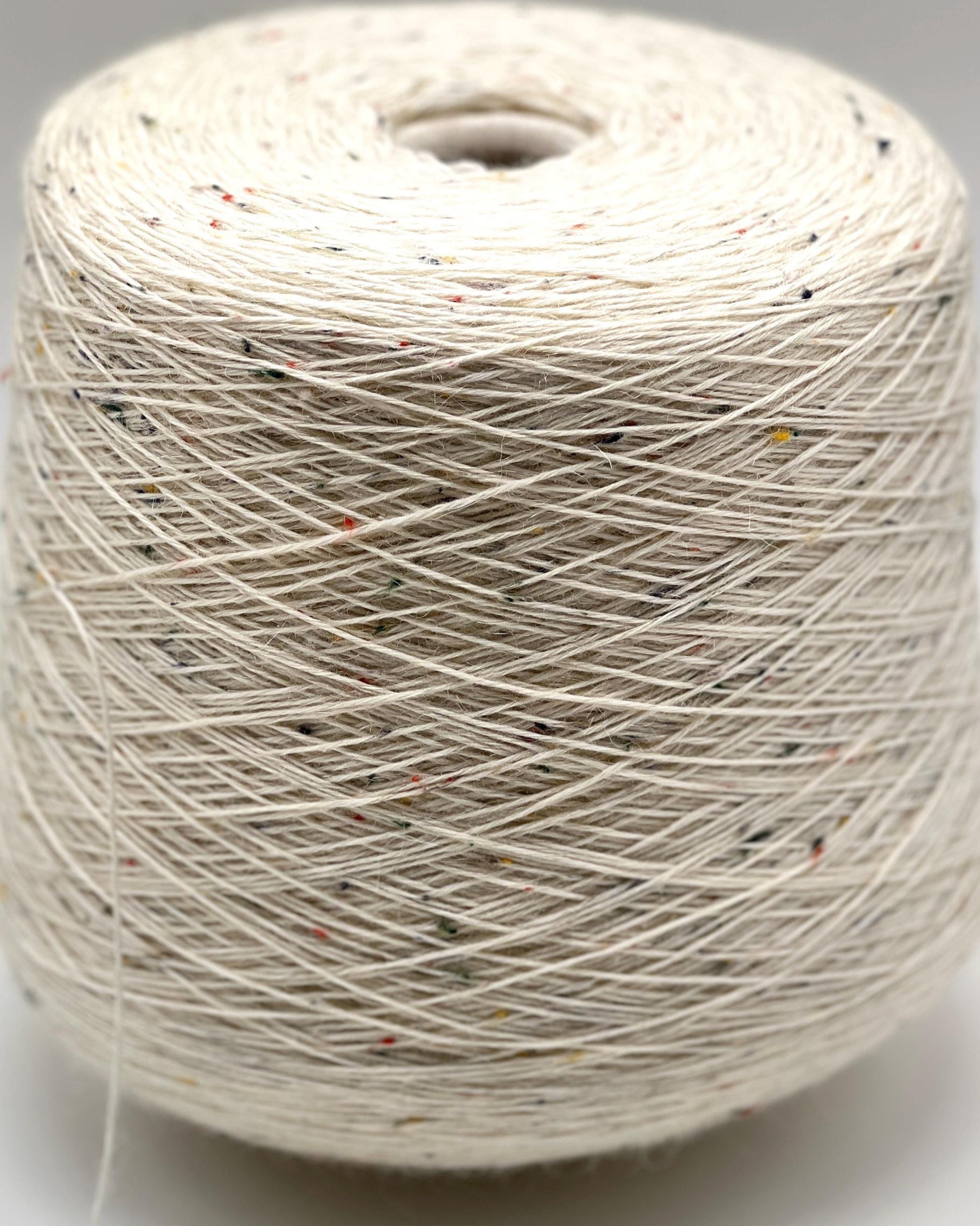 Spool of white yarn with specks on a gray background