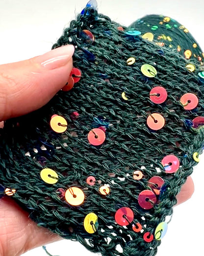 Hand holding a green knitted item with colorful sequins on a white background