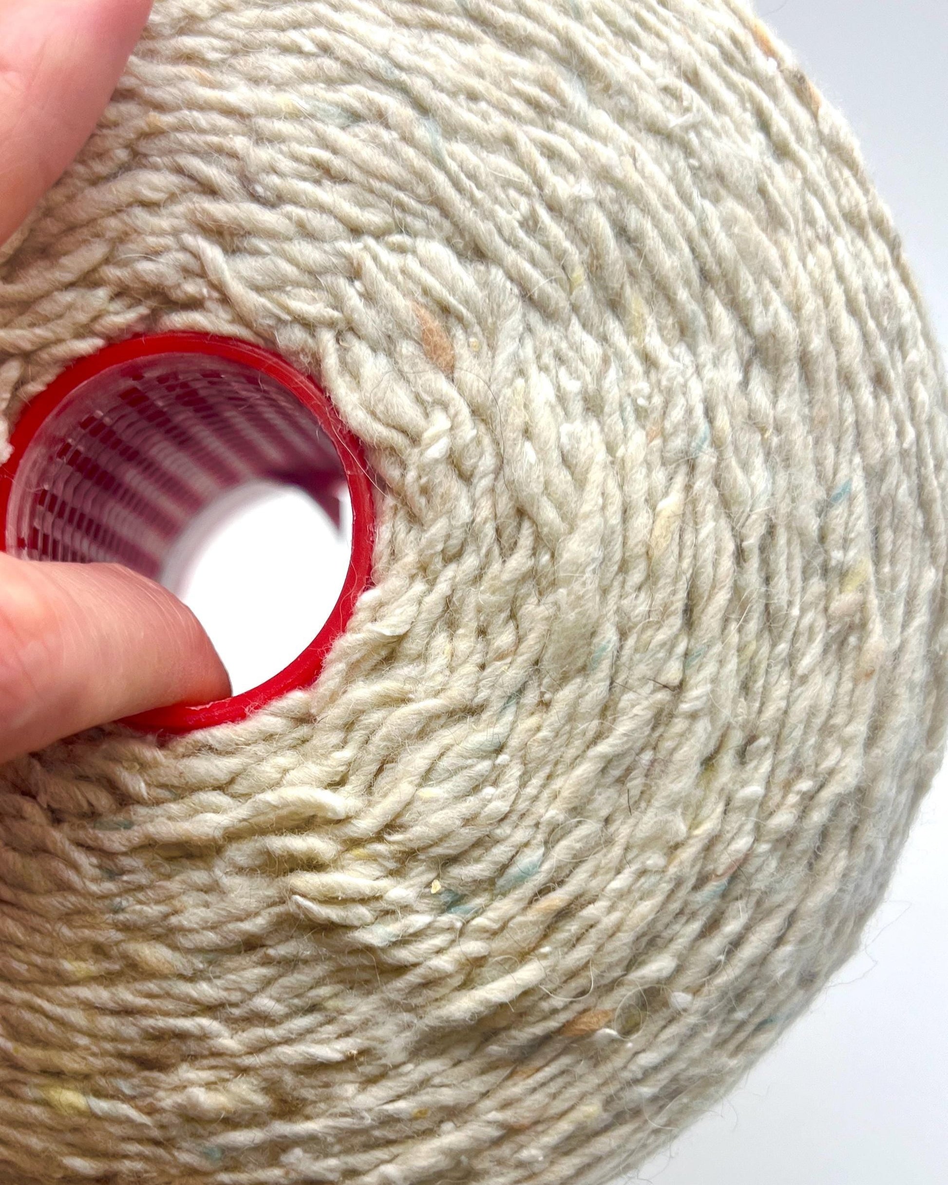 Close-up of a spool of yarn with a red plastic cap, held by a hand.
