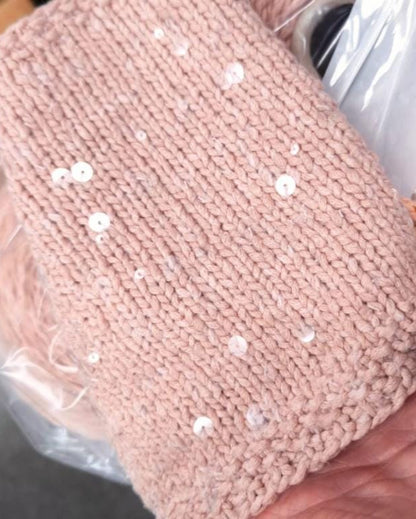 Pink knitted item with sequins held by a hand, wrapped in clear plastic.
