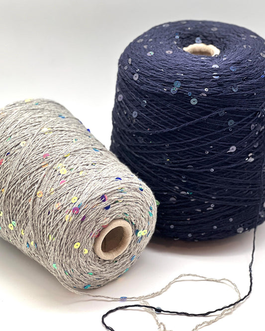 Two spools of yarn, one gray with colorful specks and one navy blue with sequins, on a white background.