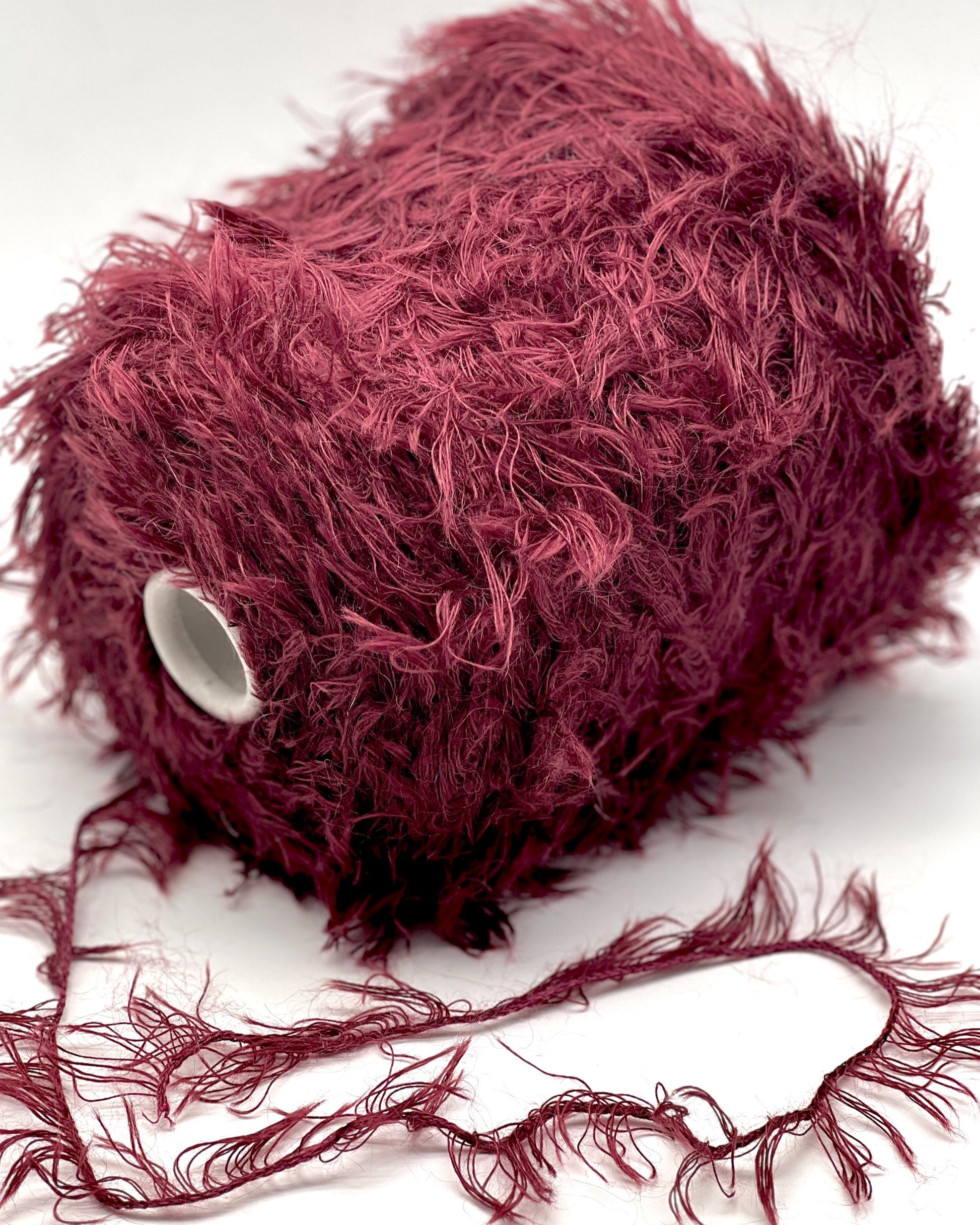 Maroon yarn ball with loose strands on a white background