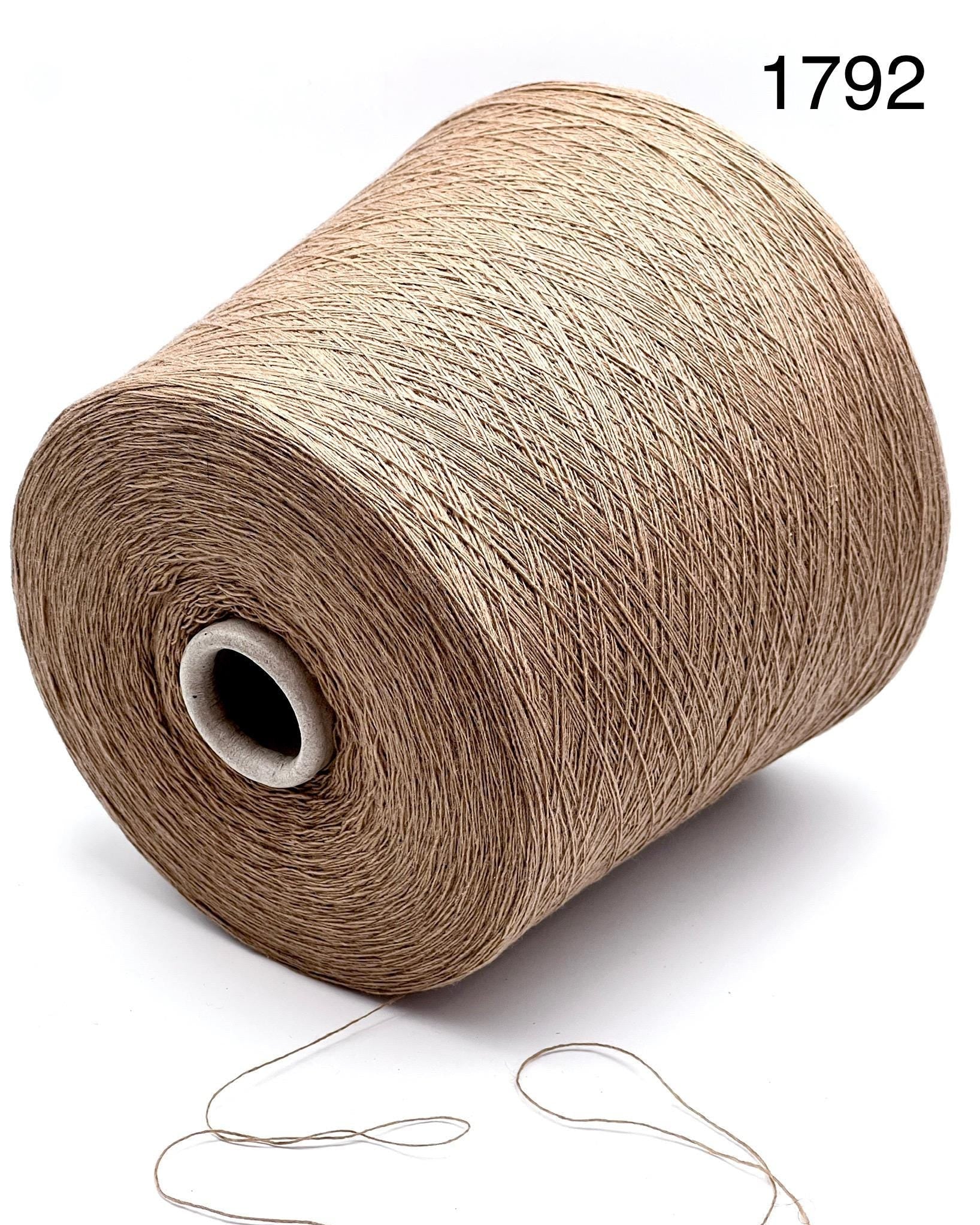 Spool of beige yarn with a needle on a white background