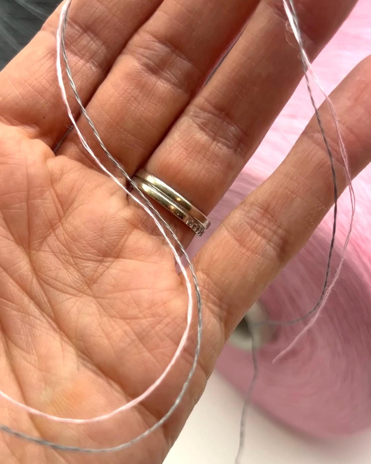 Hand wearing a gold ring with clear string wrapped around it on a pink background