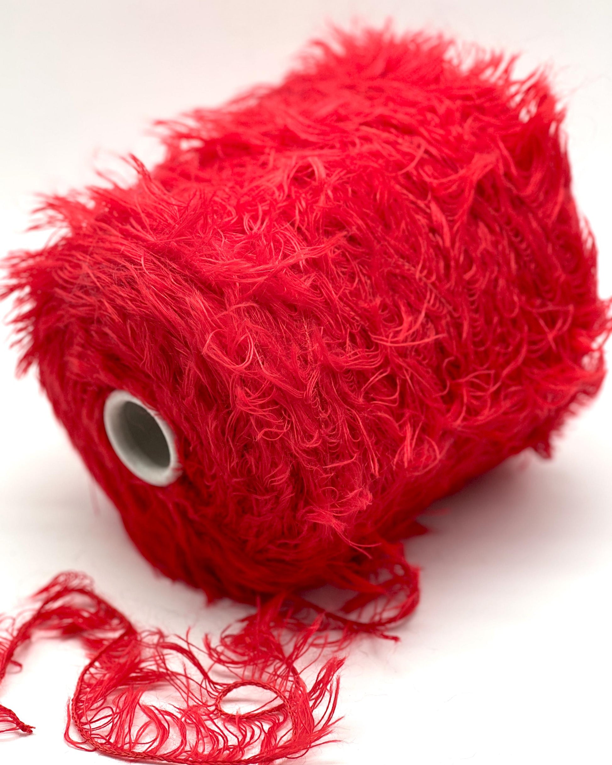 Red yarn ball with loose strands on a white background