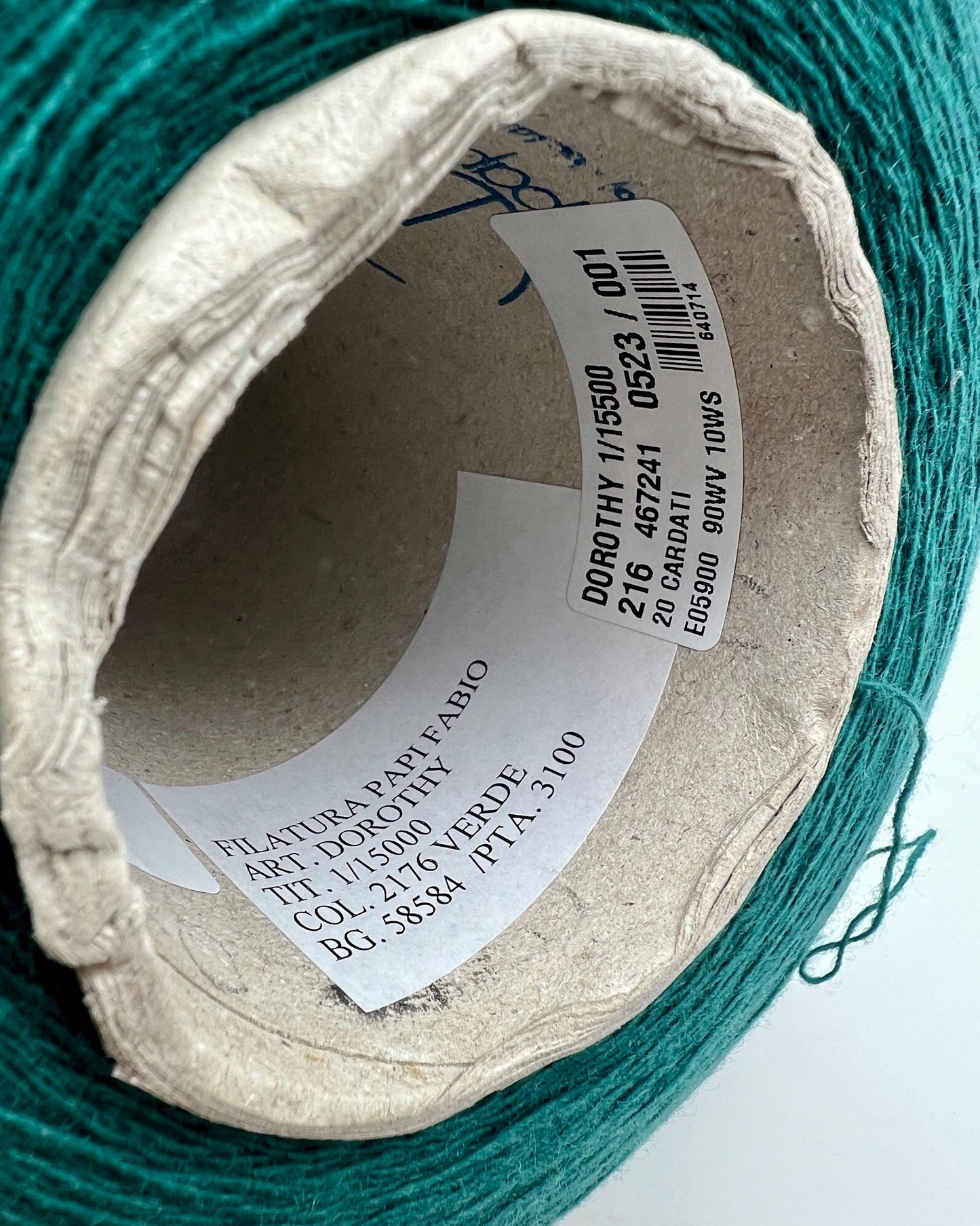 Close-up of a spool of green yarn with a label on a white background