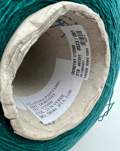 Close-up of a spool of green yarn with a label on a white background
