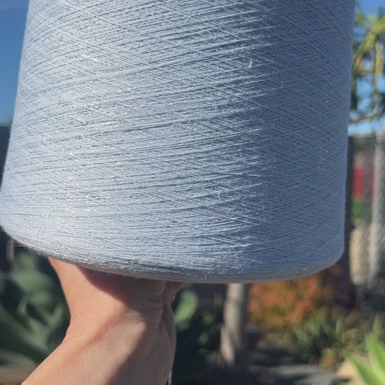 A luxurious cone of Pecci Filati SHIMMER yarn, a modern 50% Cotton, 25% Linen, 14% Polyester, and 12% Polyamide (Lurex) blend. The image showcases the refined metallic glow and delicate texture of this 3400m/100g Italian extrafine yarn, ideal for high-end blending. Authentic luxury fiber available at iDOKNiT.com.