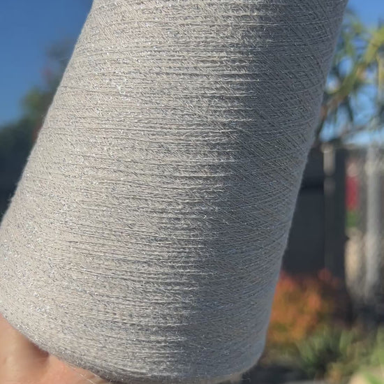 A luxurious cone of Pecci Filati SHIMMER yarn, a modern 50% Cotton, 25% Linen, 14% Polyester, and 12% Polyamide (Lurex) blend. The image showcases the refined metallic glow and delicate texture of this 3400m/100g Italian extrafine yarn, ideal for high-end blending. Authentic luxury fiber available at iDOKNiT.com.