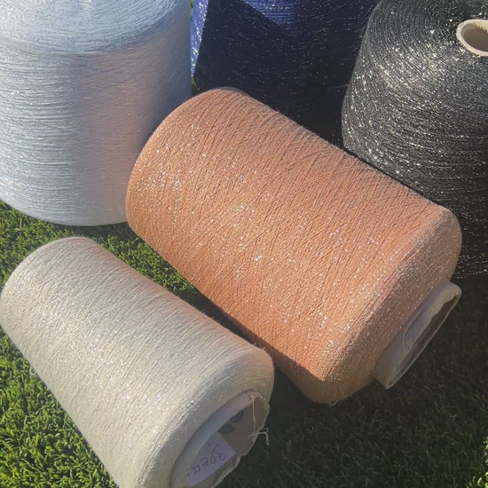 A luxurious cone of Pecci Filati SHIMMER yarn, a modern 50% Cotton, 25% Linen, 14% Polyester, and 12% Polyamide (Lurex) blend. The image showcases the refined metallic glow and delicate texture of this 3400m/100g Italian extrafine yarn, ideal for high-end blending. Authentic luxury fiber available at iDOKNiT.com.