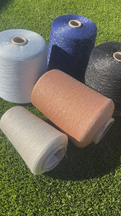 A luxurious cone of Pecci Filati SHIMMER yarn, a modern 50% Cotton, 25% Linen, 14% Polyester, and 12% Polyamide (Lurex) blend. The image showcases the refined metallic glow and delicate texture of this 3400m/100g Italian extrafine yarn, ideal for high-end blending. Authentic luxury fiber available at iDOKNiT.com.