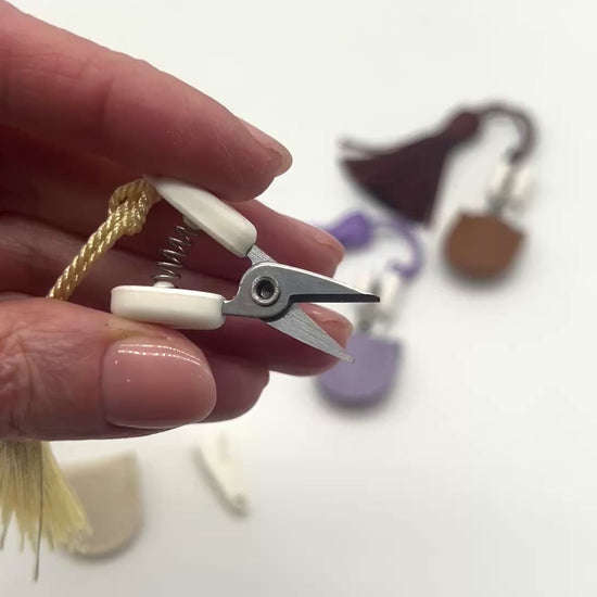 Professional iDOKNiT mini precision thread scissors for crafters. These 42mm spring-style snips feature a decorative tassel and protective cover, designed for sharp, precise trimming of yarn and embroidery floss. Compact and travel-ready accessory curated by iDOKNiT for knitting, crochet, and sewing project bags.