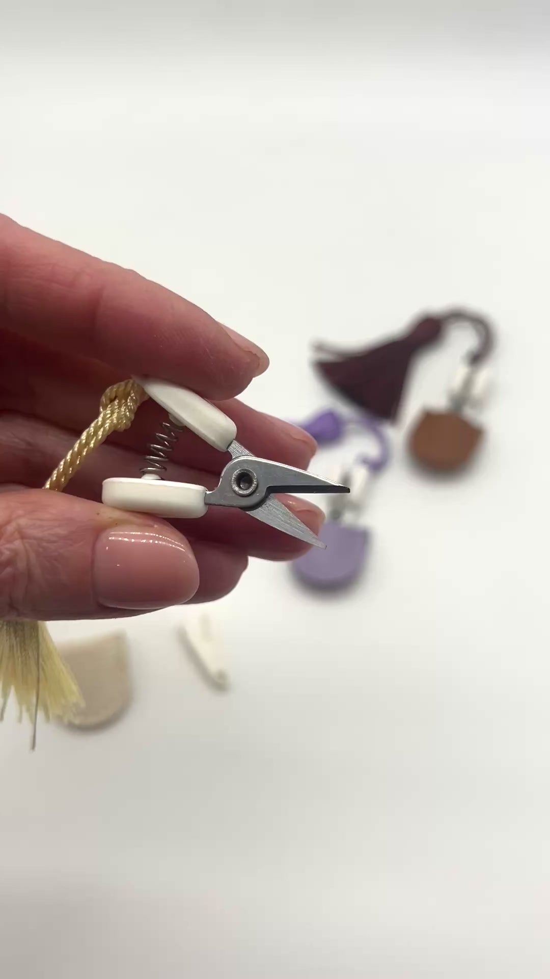 Professional iDOKNiT mini precision thread scissors for crafters. These 42mm spring-style snips feature a decorative tassel and protective cover, designed for sharp, precise trimming of yarn and embroidery floss. Compact and travel-ready accessory curated by iDOKNiT for knitting, crochet, and sewing project bags.