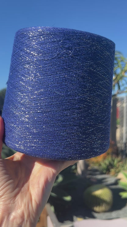 A luxurious cone of Pecci Filati SHIMMER yarn, a modern 50% Cotton, 25% Linen, 14% Polyester, and 12% Polyamide (Lurex) blend. The image showcases the refined metallic glow and delicate texture of this 3400m/100g Italian extrafine yarn, ideal for high-end blending. Authentic luxury fiber available at iDOKNiT.com.