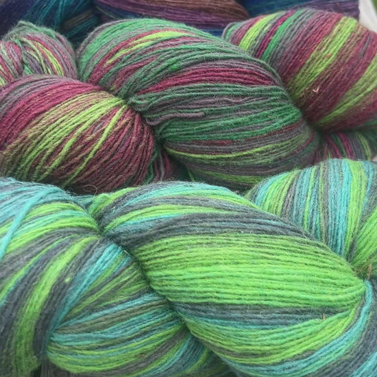 Small-batch dyed skeins of 100% Latvian Dark-Headed Sheep Wool in varied earth tones and vibrant multi-colors like Green-Brown striped 052. The rustic single-ply texture is shown in detail, including images of the sheep and the historic Paces Vilnas Fabrika origin. Available at iDOKNiT.com.