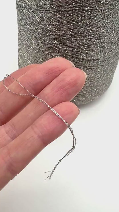 A professional cone of Kyototex MANNA-GROSSA metallic lamé yarn in Brushed Gold. The image shows the yarn's intense shimmer and fine texture, with detail shots of the fiber being held to demonstrate its lace-weight scale. Available at iDOKNiT.com.