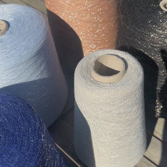 A luxurious cone of Pecci Filati SHIMMER yarn, a modern 50% Cotton, 25% Linen, 14% Polyester, and 12% Polyamide (Lurex) blend. The image showcases the refined metallic glow and delicate texture of this 3400m/100g Italian extrafine yarn, ideal for high-end blending. Authentic luxury fiber available at iDOKNiT.com.