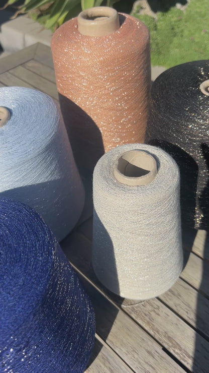 A luxurious cone of Pecci Filati SHIMMER yarn, a modern 50% Cotton, 25% Linen, 14% Polyester, and 12% Polyamide (Lurex) blend. The image showcases the refined metallic glow and delicate texture of this 3400m/100g Italian extrafine yarn, ideal for high-end blending. Authentic luxury fiber available at iDOKNiT.com.